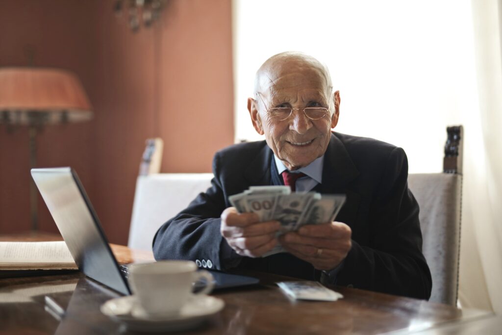 Older gentleman holding cash in his hands while sitting at his computer - How to make money taking online surveys.