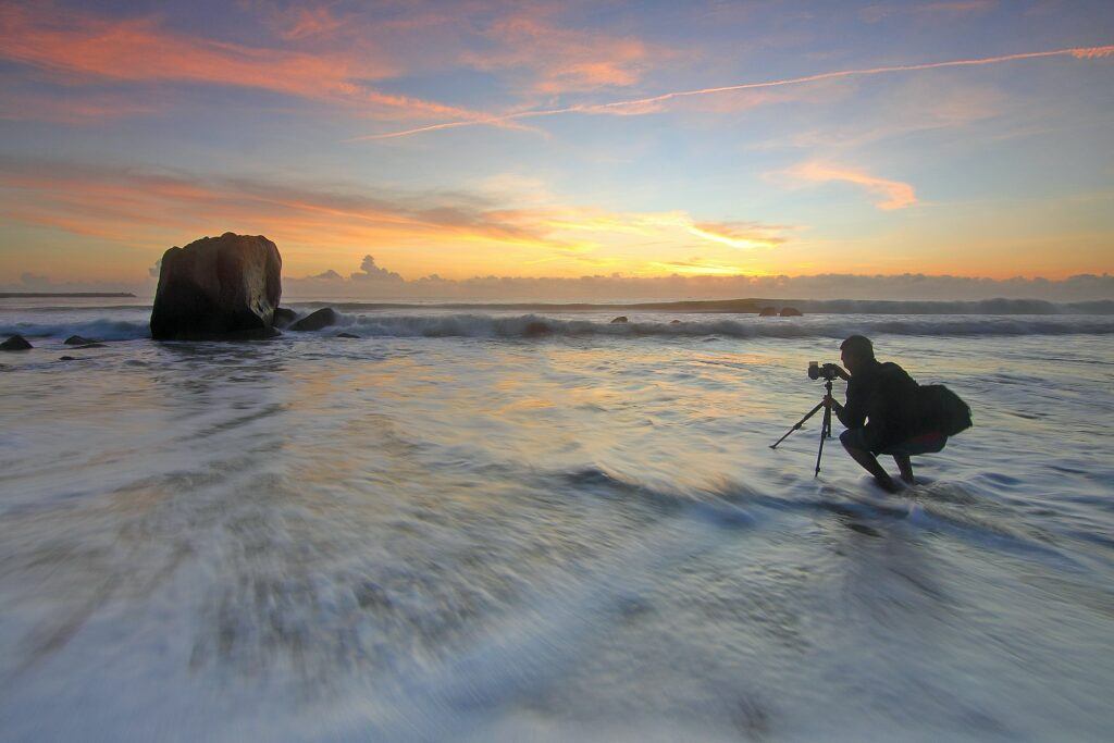 Create your own profitable online photography business - Lady standing in the water taking pictures of the waves at the beach