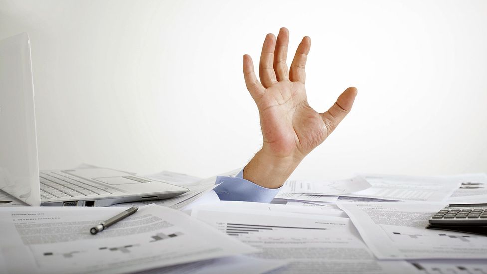 what about a side hustel? - man's hand reaching up from a pile of paper work stacked on his desk because he didn't delegate 