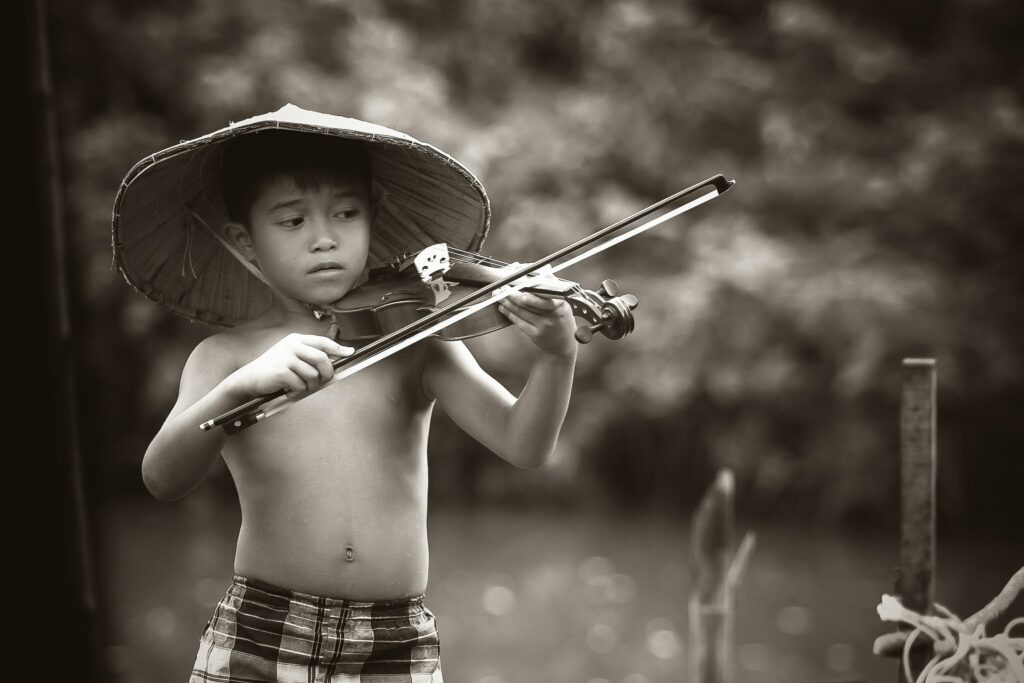 make money from your passion for music - asian boy playing the violin next to the river