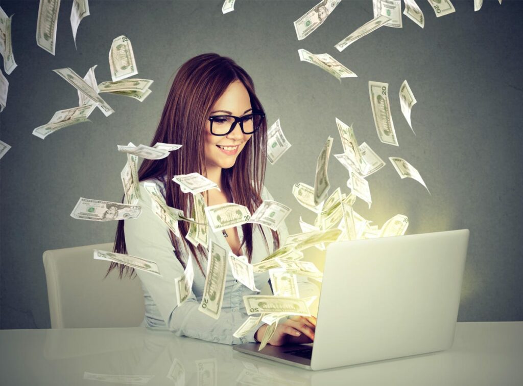 Lady sitting at her desk with money flying out of her laptop