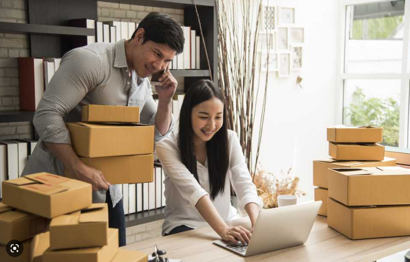 A couple boxing up products for shipping while the wife is running the business from her laptop