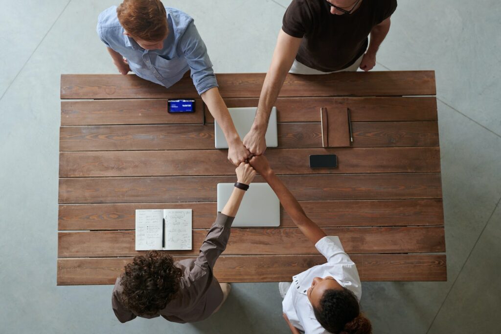 Best business entity for affiliate marketers - four people standing across a table from each other bumping fists as they agree to become partners