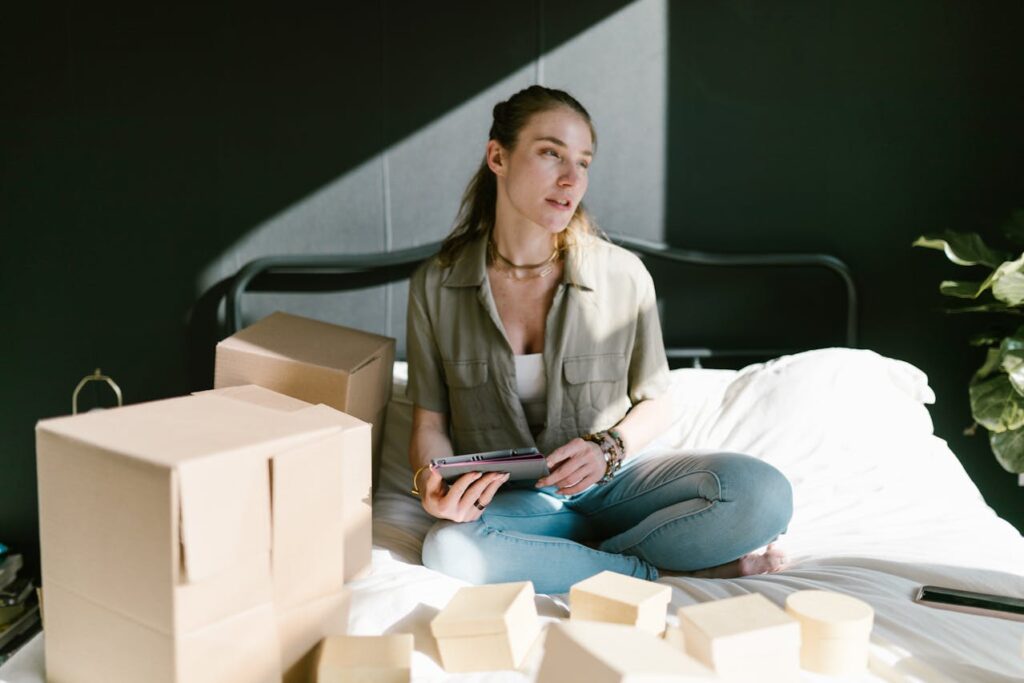 How to scale your ecommerce business - A young lady on her bed checking orders from her ecommerce business on her tablet while packing boxes for shipping